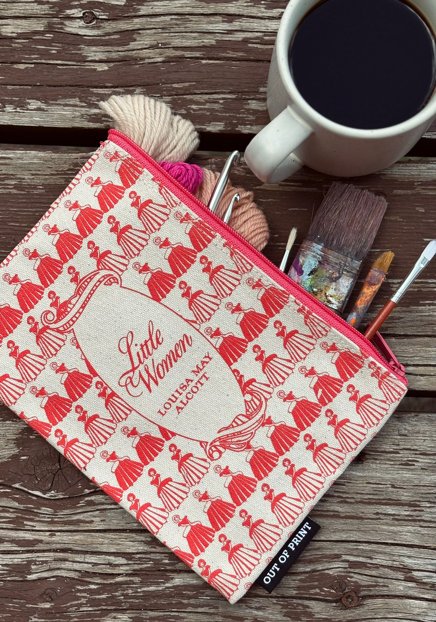 Fabric pouch with 'Little Women' design on a wooden surface with a cup of coffee and craft supplies.