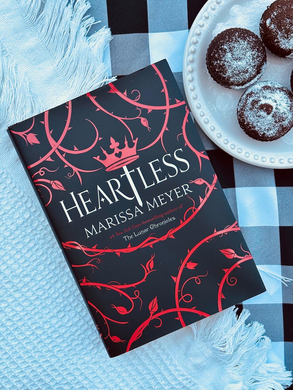 Book titled 'Heartless' by Marissa Meyer on a checkered tablecloth with pastries.